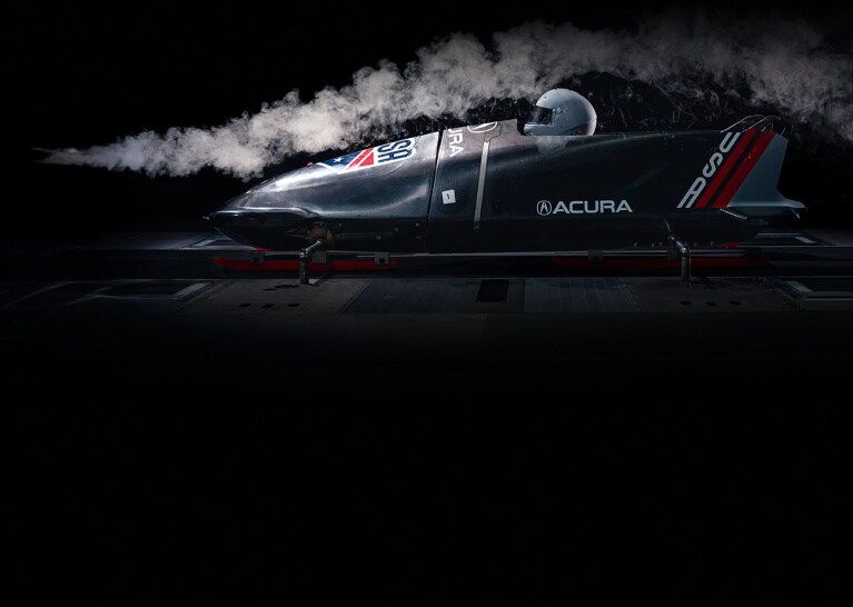 Acura USA bobsled in profile view undergoing wind tunnel testing with smoke stream.