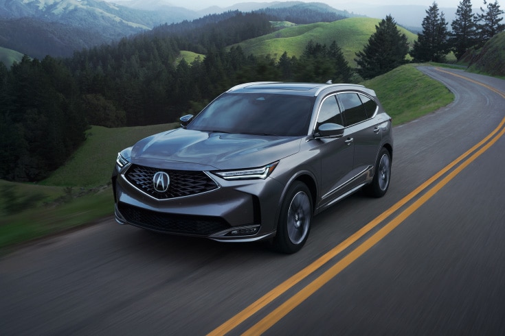 2026 Acura MDX with Advance Package in Liquid Carbon Metallic, driving on the road in a three-quarter view (Premium Performance SUV).