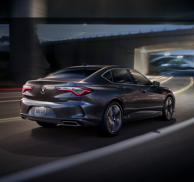 Acura 2023 TLX in Modern Steel Metallic driving at night, 3/4 rear view