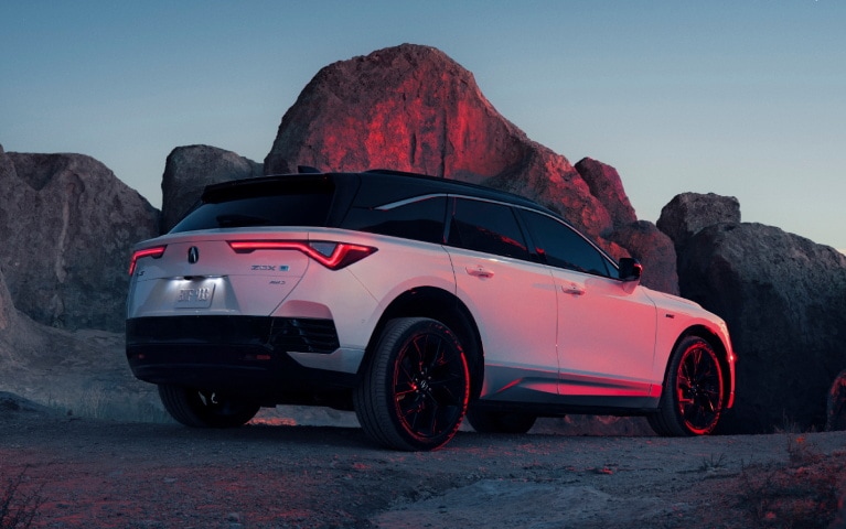 2024 Acura ZDX Type S in Snowfall Pearl rear view in a rocky background at sundown.
