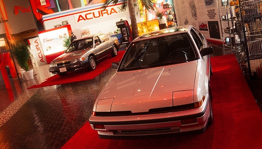 Acura 1986 model parked on a red carpet inside a bright automotive showroom.