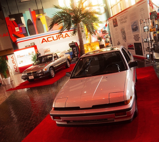 Acura 1986 model parked on a red carpet inside a bright automotive showroom.