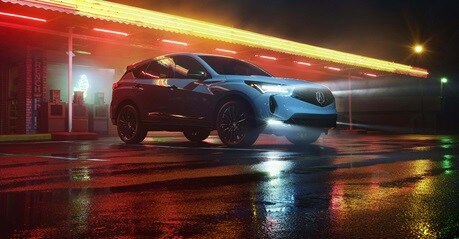 2026 Acura RDX in Urban Gray Pearl front parked at a neon-lit diner at night (Premium Sport Crossover SUV).